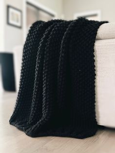 black knitted blanket sitting on the floor next to a white couch in a living room