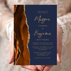 a person holding up a wedding card with gold foil on the front and back side