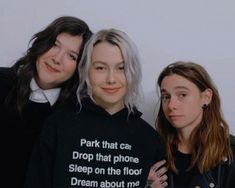 three women standing next to each other in front of a white wall with the words park that car drop that phone sleep on the floor dream about me