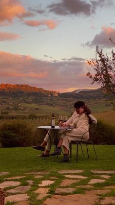 a woman sitting at a table with a bottle of wine in front of her on the grass