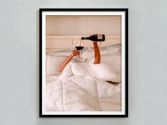 a man laying in bed drinking from a wine glass with his feet up on the pillow