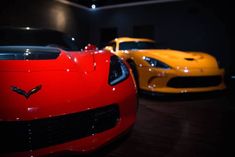 two yellow and one red sports cars in a dark room with lights on the ceiling