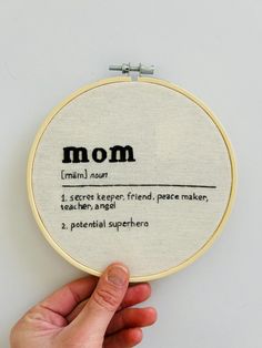 a hand is holding up a cross stitch hoop with the word mom written on it