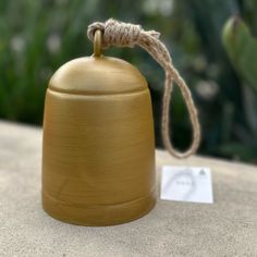 a golden bell sitting on top of a table next to a tag and some plants