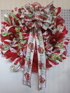 a red and white christmas wreath hanging on the wall with ribbon around it's center