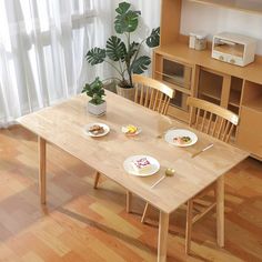 a wooden table with two plates of food on it next to a potted plant