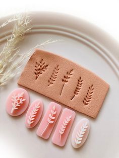 three different types of nail art on a plate next to some wheat stalks and leaves