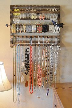 a rack with many necklaces hanging from it and a lamp on the wall behind it