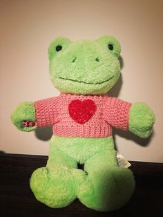 a green stuffed animal with a heart on it's chest sitting on a table