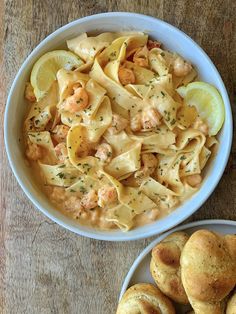 two bowls filled with pasta and shrimp next to rolls