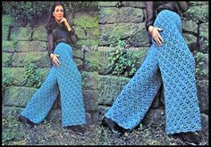 a woman wearing blue crocheted pants standing next to a stone wall