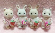 three little stuffed animals sitting next to each other on a pink surface with one holding a strawberry