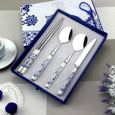 a set of four silverware in a box with blue and white flowers on the table