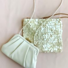 a white purse sitting on top of a pink surface next to a handbag with sequins