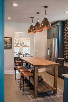 a kitchen with a wooden table surrounded by stools and pendant lights over the island