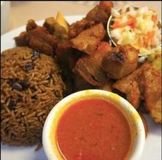 a white plate topped with meat and rice next to a bowl of dipping sauce on top of it