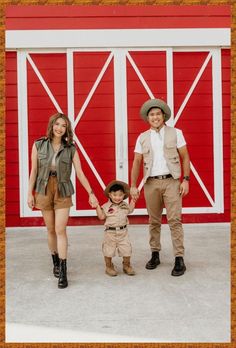 a man, woman and child are standing in front of a red barn holding hands