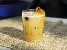 a drink with an orange garnish on the rim sits on a burlap cloth