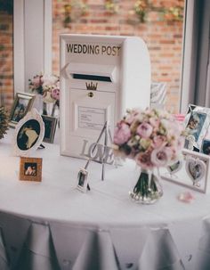 a white table with flowers and pictures on it in front of a brick wall that says wedding post