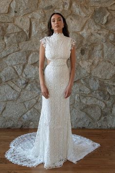 a woman standing in front of a stone wall wearing a white wedding dress with an open back