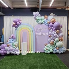 balloon arch with balloons and rainbows on display in front of a backdrop that says always turns 4