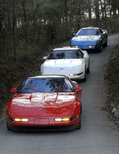 three cars are lined up on the side of a road in front of some trees