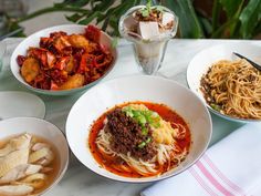 several bowls of food on a table with chopsticks and utensils next to them