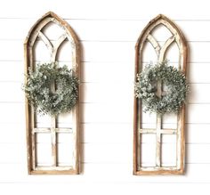 two old windows with wreaths on them against a white wall in the shape of an arched window