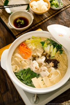 a white bowl filled with soup and vegetables on top of a wooden table next to chopsticks