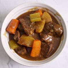 a white bowl filled with stew and carrots on top of a marble countertop