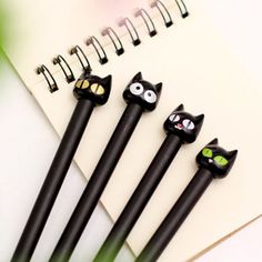 five black cat shaped pens sitting on top of a notepad