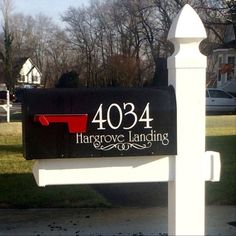 a black and white mailbox sitting on the side of a road in front of a house