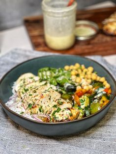 a black bowl filled with chicken and vegetables next to a jar of dressing on a table