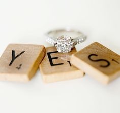 a engagement ring sitting on top of scrabble blocks with the word yes spelled out