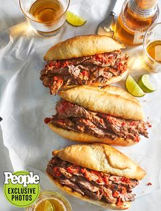 three sandwiches sitting next to each other on top of a white paper with lime wedges