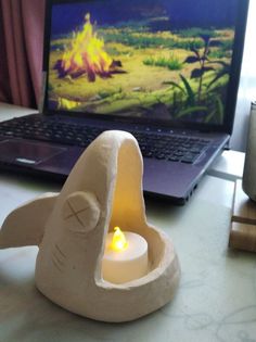 a laptop computer sitting on top of a desk next to a small candle holder with a lit candle in the shape of a bird