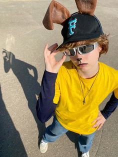 a young boy wearing sunglasses and a hat with ears on his head, standing in an empty parking lot