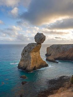 a rock formation in the middle of the ocean next to a cliff with a large rock sticking out of it's side