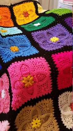 a crocheted blanket with many different colors and designs on it, sitting on a bed