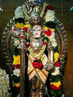 a statue of the hindu god person with two swords and flowers around his neck, standing in front of a wall