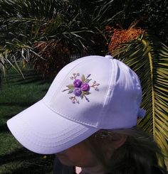 a woman wearing a white hat with purple flowers on it and palm trees in the background