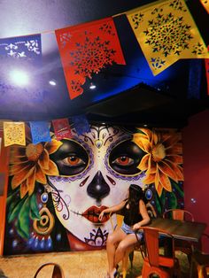 a woman sitting at a table in front of a wall with flowers painted on it