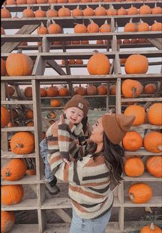 a woman holding a small child in front of pumpkins on display at a farm