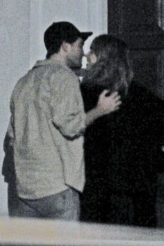 two people standing next to each other in front of a door and one person kissing the other