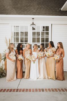 a group of women standing next to each other in front of a white house holding bouquets