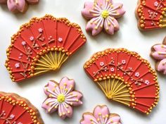 decorated cookies with pink and yellow decorations on top of a white countertop next to red fan shaped cookies