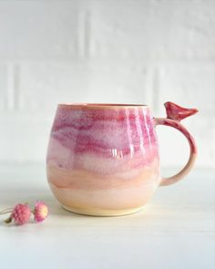 a pink and white coffee cup with a bird on the handle next to some flowers