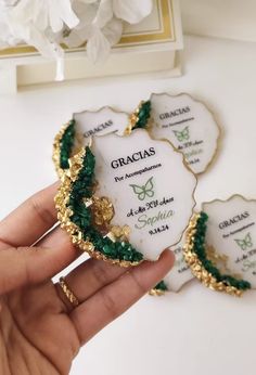 a hand holding some white and green brooches with gold trimming on them