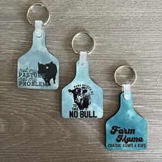 three keychains with different designs on them sitting on a wooden surface, one is blue and the other has black print