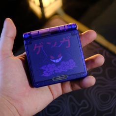 a hand holding a small purple object with an evil face on it's side